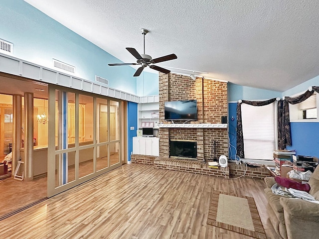 unfurnished living room with a fireplace, ceiling fan, brick wall, light hardwood / wood-style flooring, and a textured ceiling