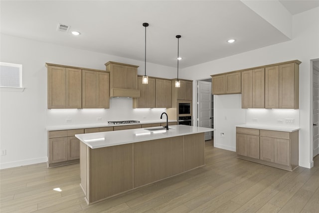 kitchen with stainless steel gas stovetop, a kitchen island with sink, light hardwood / wood-style flooring, decorative light fixtures, and sink