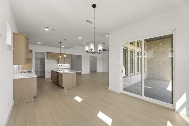 kitchen with an inviting chandelier, a center island with sink, hanging light fixtures, and light wood-type flooring