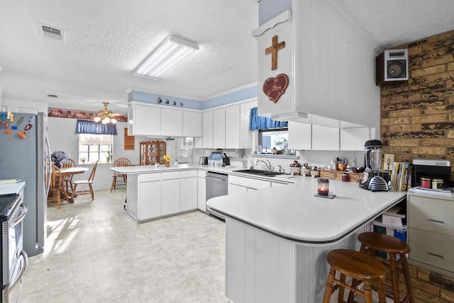 kitchen with appliances with stainless steel finishes, white cabinetry, a kitchen breakfast bar, kitchen peninsula, and a textured ceiling