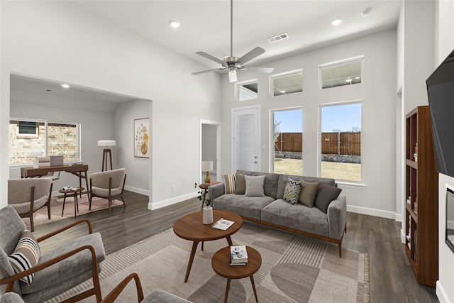 living room with a high ceiling, ceiling fan, plenty of natural light, and dark hardwood / wood-style flooring