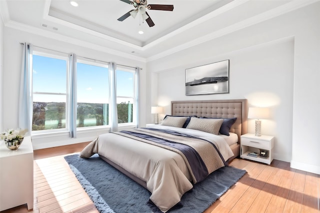 bedroom with crown molding, light hardwood / wood-style flooring, a raised ceiling, and ceiling fan