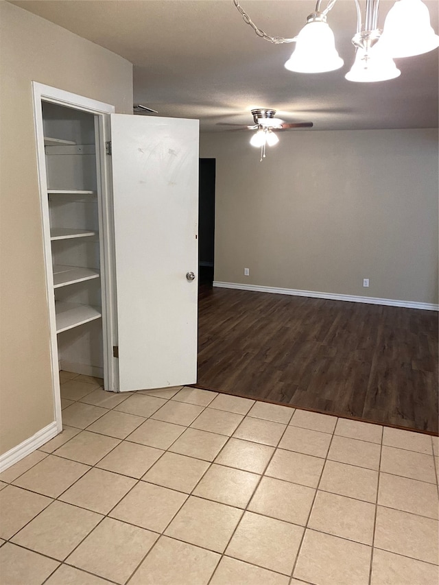 tiled spare room with ceiling fan with notable chandelier