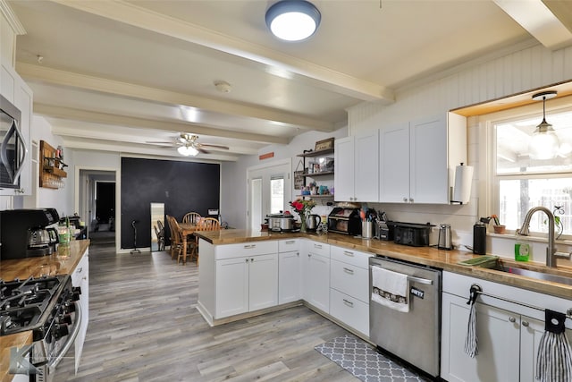 kitchen featuring stainless steel appliances, white cabinetry, sink, beamed ceiling, and ceiling fan