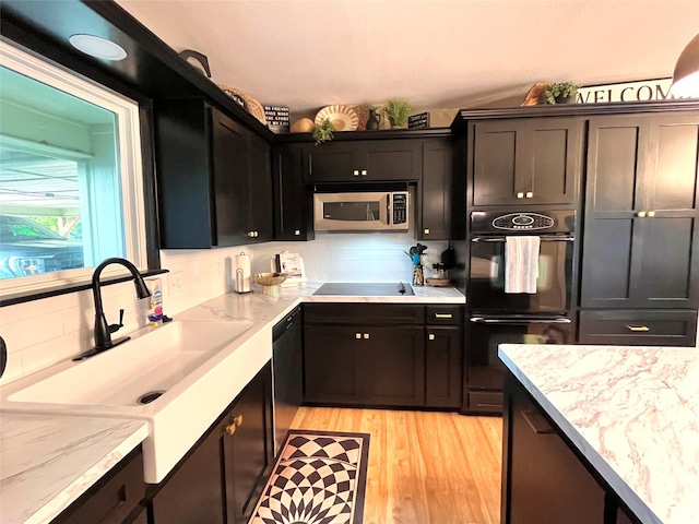 kitchen featuring tasteful backsplash, sink, light stone counters, black appliances, and light hardwood / wood-style flooring