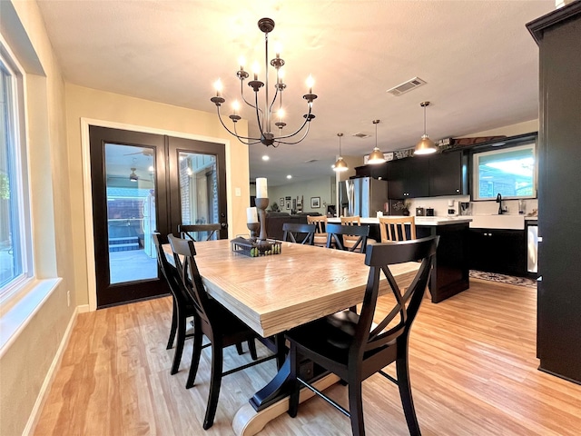 dining area with a notable chandelier, sink, light hardwood / wood-style flooring, and french doors