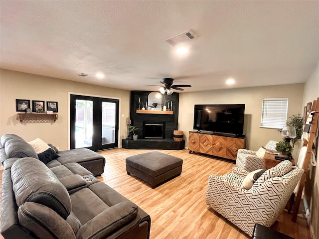 living room featuring hardwood / wood-style flooring, ceiling fan, a textured ceiling, a brick fireplace, and french doors