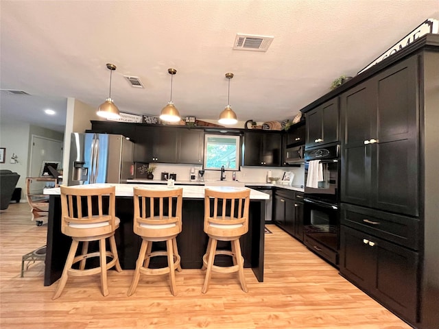 kitchen with a breakfast bar area, stainless steel fridge with ice dispenser, light wood-type flooring, double oven, and a kitchen island