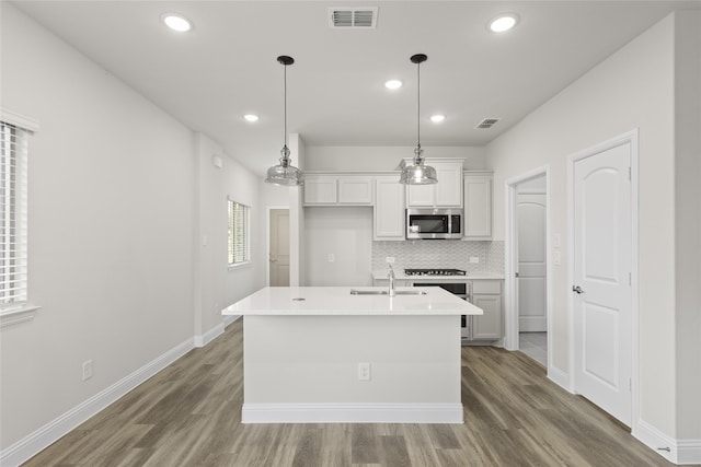 kitchen featuring decorative light fixtures, sink, white cabinets, decorative backsplash, and a center island with sink