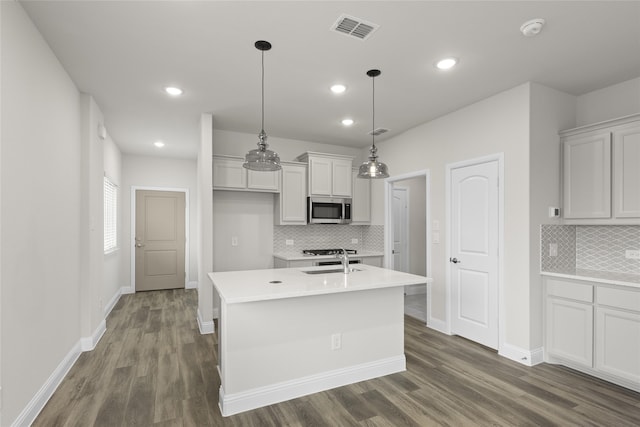 kitchen featuring decorative light fixtures, white cabinetry, sink, dark wood-type flooring, and a center island with sink