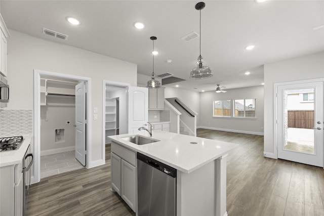 kitchen with sink, hanging light fixtures, a center island with sink, stainless steel appliances, and backsplash