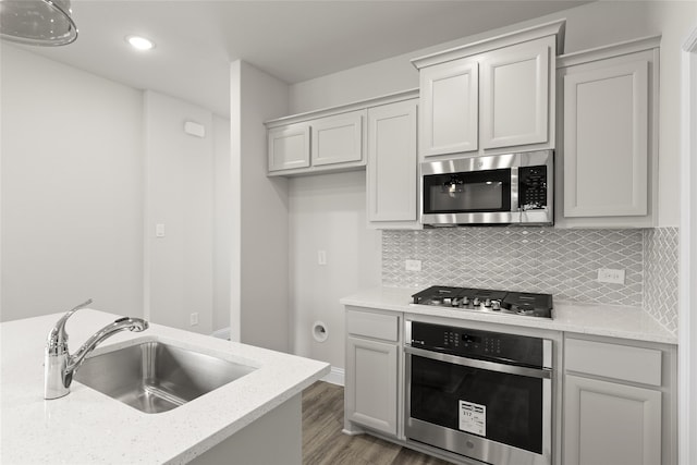 kitchen featuring sink, appliances with stainless steel finishes, light stone countertops, light hardwood / wood-style floors, and decorative backsplash