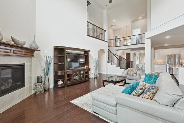 living room featuring a tiled fireplace, a high ceiling, and dark hardwood / wood-style floors