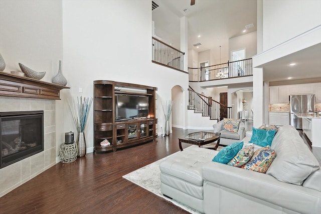 living room featuring a tiled fireplace, dark wood-type flooring, and a high ceiling