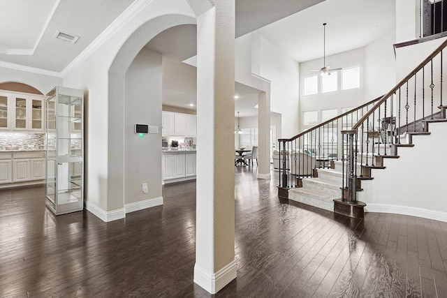 foyer entrance with ceiling fan, ornamental molding, dark hardwood / wood-style floors, and a towering ceiling