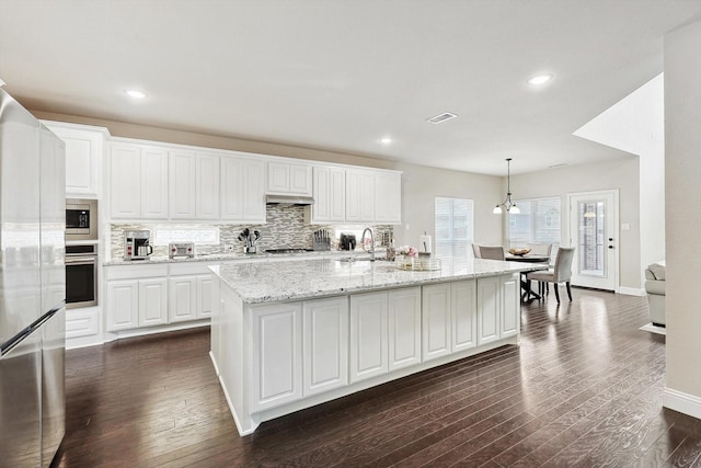 kitchen featuring stainless steel appliances, an island with sink, hanging light fixtures, and white cabinets