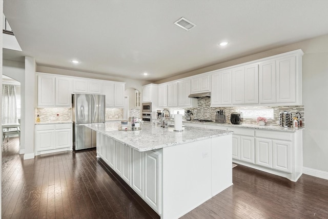 kitchen with appliances with stainless steel finishes, a center island with sink, white cabinets, and light stone counters