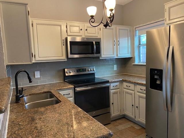 kitchen featuring sink, appliances with stainless steel finishes, dark stone countertops, white cabinets, and decorative backsplash