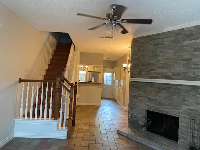 staircase with a large fireplace, ceiling fan with notable chandelier, and a textured ceiling