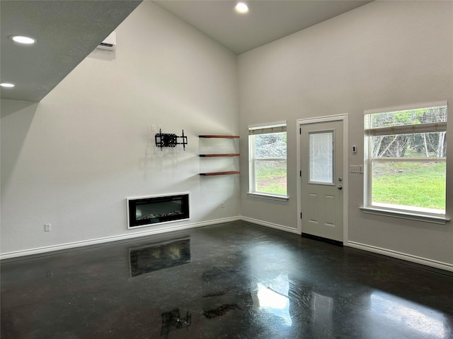 334 Fort Graham Rd, Whitney, TX 76692 - unfurnished living room with finished concrete flooring, recessed lighting, a glass covered fireplace, baseboards, and a high ceiling