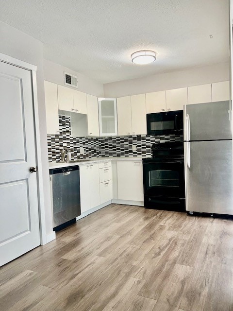 kitchen with light hardwood / wood-style floors, appliances with stainless steel finishes, white cabinets, and backsplash