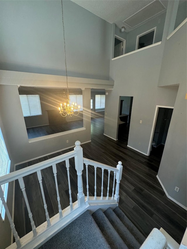 staircase with wood-type flooring, a towering ceiling, a textured ceiling, and an inviting chandelier