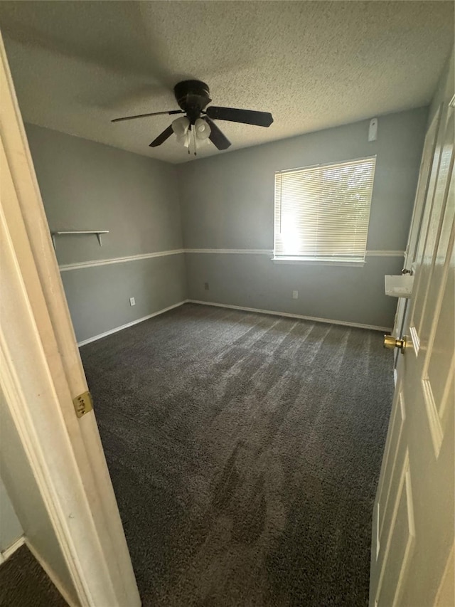 empty room featuring a textured ceiling, dark carpet, and ceiling fan