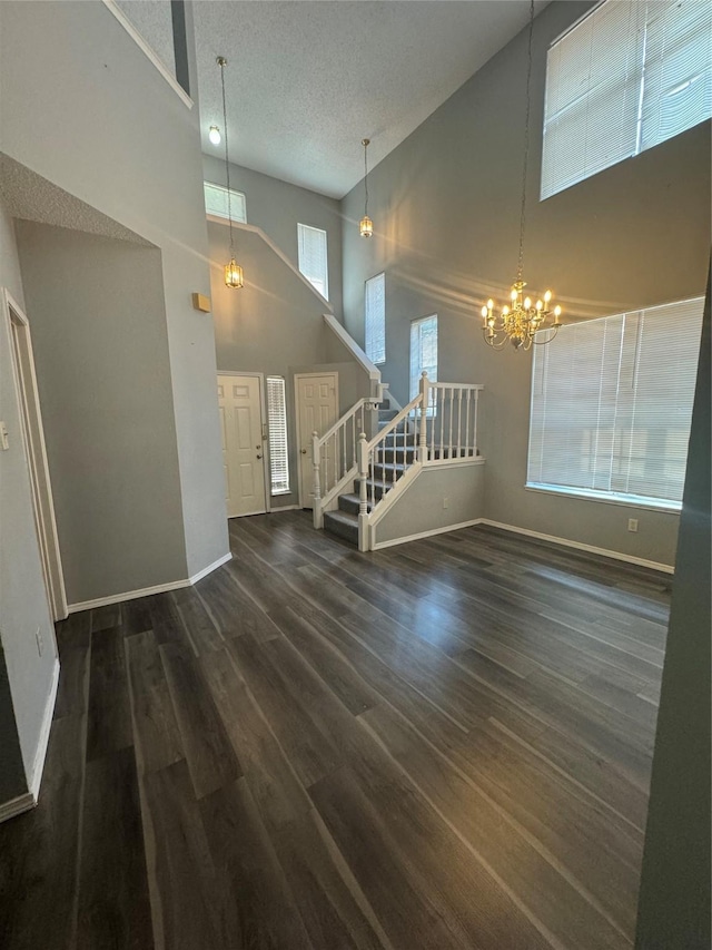 unfurnished living room with dark hardwood / wood-style floors, a textured ceiling, high vaulted ceiling, and a chandelier