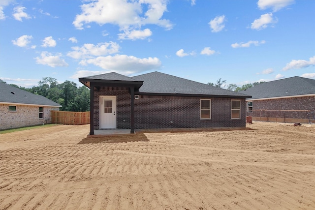 rear view of property with a shingled roof, brick siding, and fence