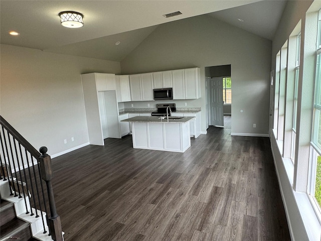 kitchen with stainless steel electric range, white cabinetry, dark hardwood / wood-style floors, light stone countertops, and an island with sink