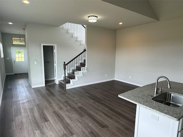 kitchen featuring sink, a high ceiling, hanging light fixtures, light stone counters, and dark wood-type flooring