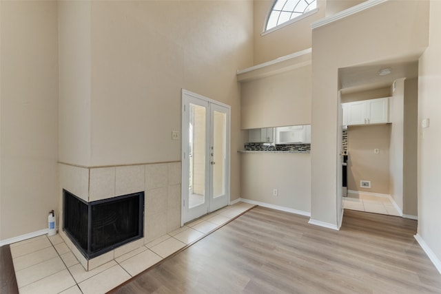 foyer entrance with a tile fireplace, french doors, light wood-type flooring, and a towering ceiling