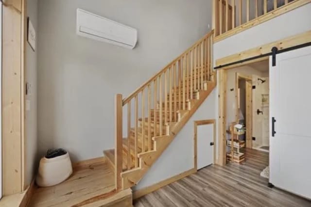 stairs with a wall mounted air conditioner, wood-type flooring, and a barn door