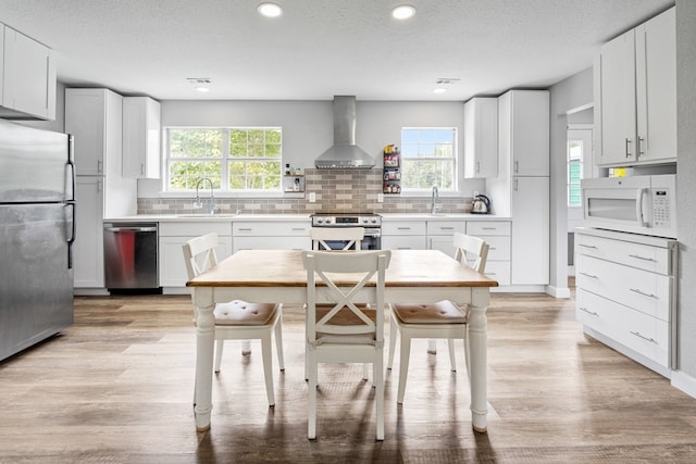 kitchen featuring appliances with stainless steel finishes, light countertops, wall chimney range hood, and white cabinetry