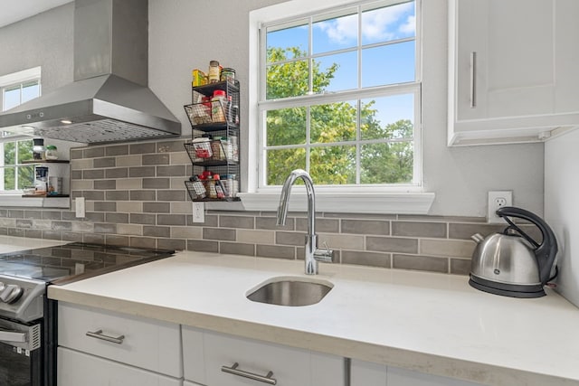 kitchen featuring stainless steel electric stove, island range hood, white cabinets, and plenty of natural light