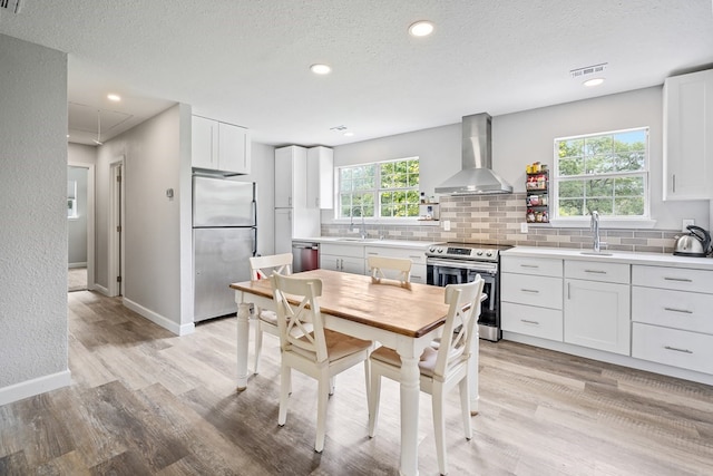 kitchen featuring appliances with stainless steel finishes, white cabinets, light wood-type flooring, and wall chimney exhaust hood