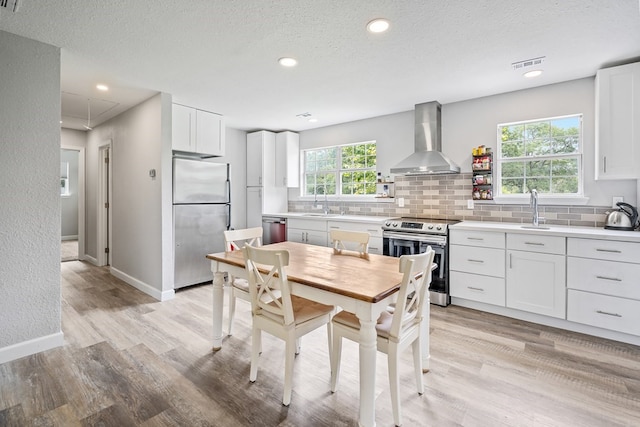 kitchen with visible vents, white cabinets, stainless steel appliances, light countertops, and wall chimney range hood