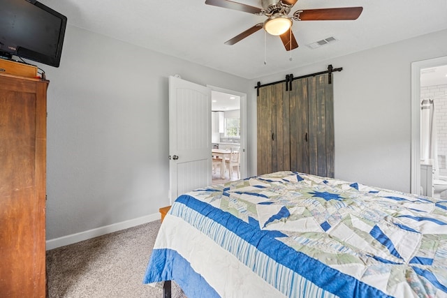 bedroom with carpet flooring, a barn door, ensuite bath, and ceiling fan