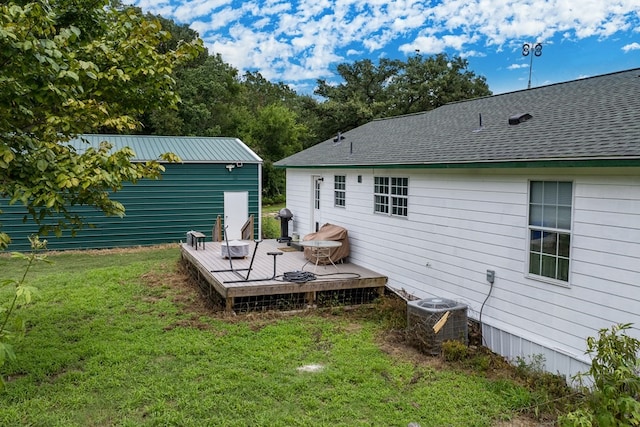 rear view of house featuring central air condition unit, roof with shingles, a deck, and a yard