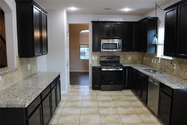 kitchen featuring light tile patterned flooring, sink, stainless steel appliances, light stone countertops, and backsplash