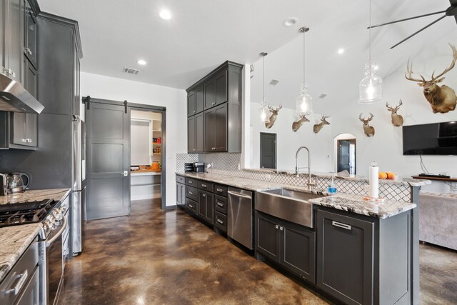 kitchen with appliances with stainless steel finishes, sink, pendant lighting, a barn door, and decorative backsplash