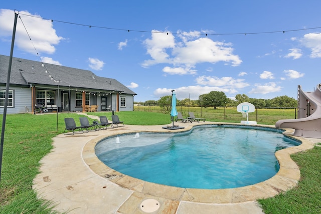 view of pool with a water slide, a patio area, and a lawn