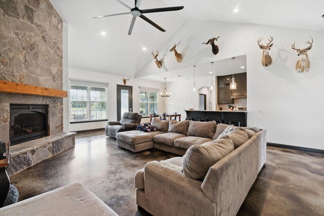 living room featuring a fireplace, concrete flooring, ceiling fan with notable chandelier, and high vaulted ceiling