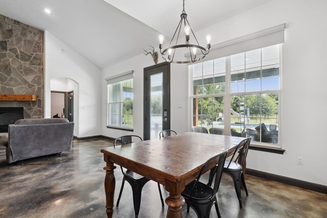 dining room with a stone fireplace, a chandelier, and lofted ceiling