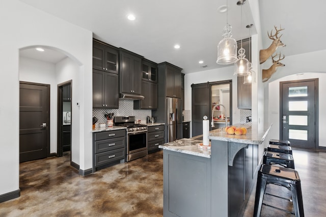 kitchen with a kitchen bar, appliances with stainless steel finishes, light stone counters, hanging light fixtures, and decorative backsplash