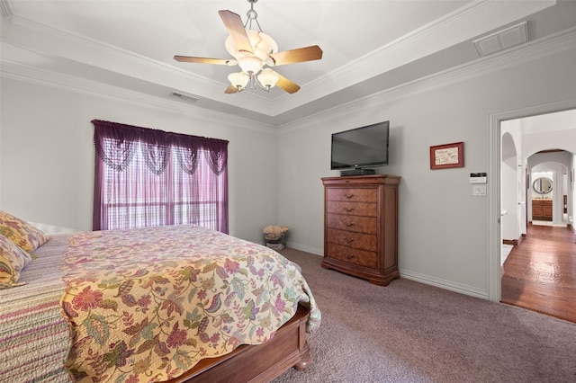 carpeted bedroom featuring arched walkways, a tray ceiling, visible vents, and crown molding