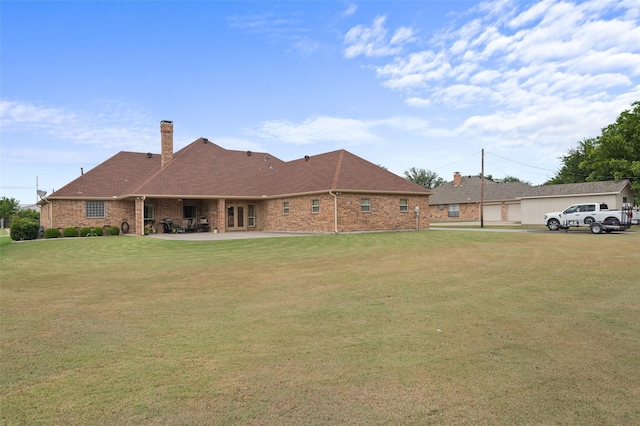 exterior space with a lawn, a chimney, an outdoor structure, a patio area, and brick siding