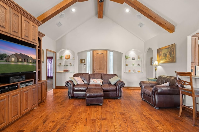 living area with beam ceiling, arched walkways, and wood finished floors