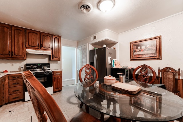kitchen featuring under cabinet range hood, visible vents, gas range, and stainless steel fridge