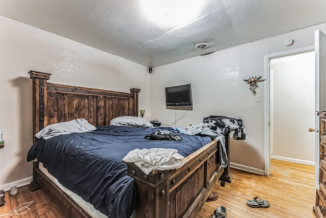 bedroom with baseboards, a textured ceiling, and light wood finished floors